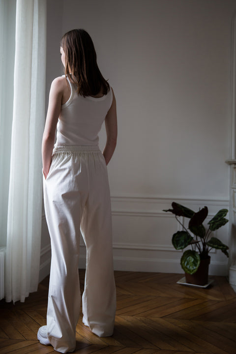Dalva is wearing White Canvas sustainable cotton stripes genderless, seasonless casual checks trousers, size M. The white cotton stripes trousers have minimal modern aesthetics design allowing comfort and bringing self-confidence. This unique piece is made locally in Paris to reduce environmental impact and guarantee high quality and durability of the products.