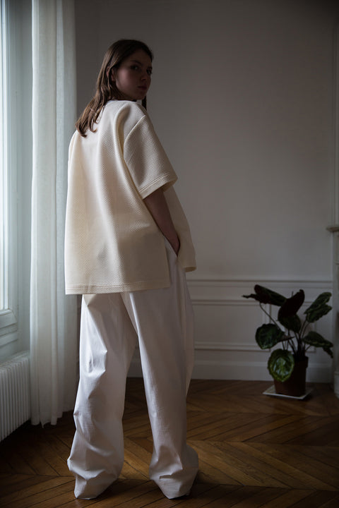 Dalva is wearing White Canvas sustainable cotton stripes genderless, seasonless casual checks trousers, size M. The white cotton stripes trousers have minimal modern aesthetics design allowing comfort and bringing self-confidence. This unique piece is made locally in Paris to reduce environmental impact and guarantee high quality and durability of the products.