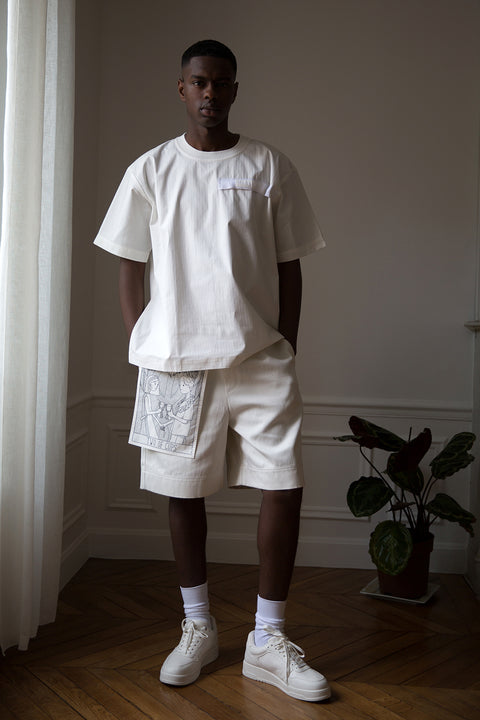 Thierno is wearing White Canvas sustainable white, oversized, genderless, seasonless t-shirt, one size. The cotton stripes t-shirt has minimal modern aesthetics design allowing comfort and bringing self-confidence. This unique piece is made locally in Paris to reduce environmental impact and guarantee high quality and durability of the products. 