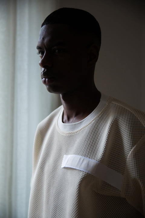 Thierno is wearing White Canvas sustainable mesh oversized, genderless, seasonless t-shirt, one size. The mesh t-shirt has minimal modern aesthetics design allowing comfort and bringing self-confidence. This unique piece is made locally in Paris to reduce environmental impact and guarantee high quality and durability of the products. 